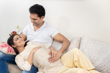Happy indian couple expecting a baby while husband touching the belly of his pregnant wife on...