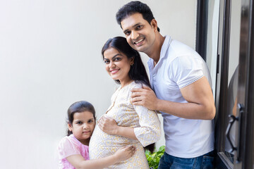 Portrait of happy indian pregnant woman with her husband and daughter at home, Awaiting for baby.