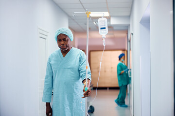 Fototapeta premium Black senior man with IV drip walking through hospital hallway.