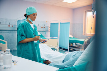 Female surgeon talks to black senior patient who is recovering in hospital ward.