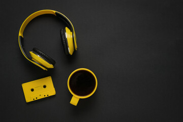 A black background with yellow headphones, a cassette tape and a cup of coffee.
