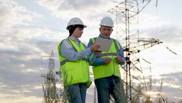 Electrician shows report on tablet to engineer walking across substation