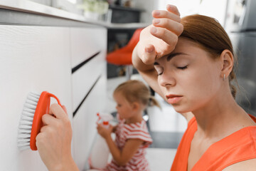 Tired woman and her daughter are brushing white kitchen cabinet