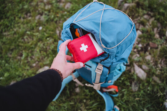 A first aid kit is in a backpack, a hand holds a bag of medicines.