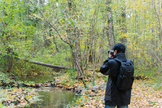 Rear view of a man in black taking pictures in a forest