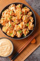 Crispy fried panko coated chicken pieces smothered in a spicy, creamy bang bang sauce closeup on the plate on the table. Vertical top view from above
