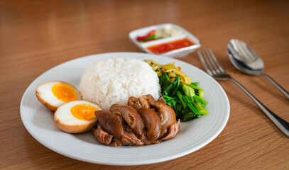 Stewed pork leg with boiled egg and rice on white plate.