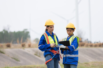 Group of female engineer working at wind turbines farm, discussing and inspecting quality wind turbines, planing maintenance of wind turbines at windmill field farm 