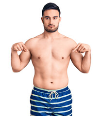 Young handsome man wearing swimwear pointing down looking sad and upset, indicating direction with...