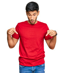 Young handsome man wearing casual red tshirt pointing down with fingers showing advertisement,...