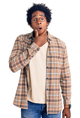 Handsome african american man with afro hair wearing casual clothes and glasses looking fascinated with disbelief, surprise and amazed expression with hands on chin