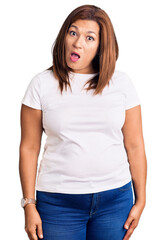 Fototapeta premium Middle age latin woman wearing casual white tshirt in shock face, looking skeptical and sarcastic, surprised with open mouth