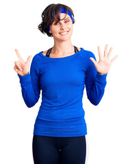 Obraz na płótnie Canvas Beautiful young woman with short hair wearing training workout clothes showing and pointing up with fingers number seven while smiling confident and happy.