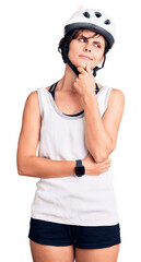 Beautiful young woman with short hair wearing bike helmet serious face thinking about question with hand on chin, thoughtful about confusing idea