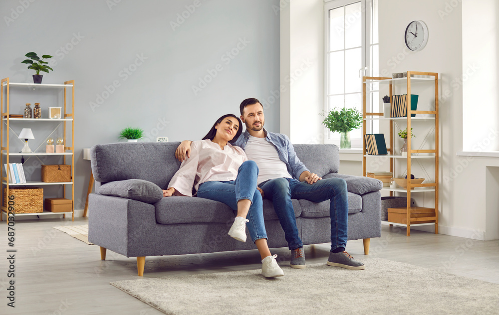 Wall mural young family couple spending time at home. happy, relaxed man and woman sitting together on a comfor