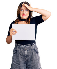 Young beautiful caucasian woman holding blank empty paper stressed and frustrated with hand on head, surprised and angry face