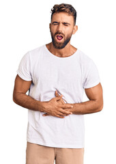 Young hispanic man wearing casual white tshirt with hand on stomach because nausea, painful disease...