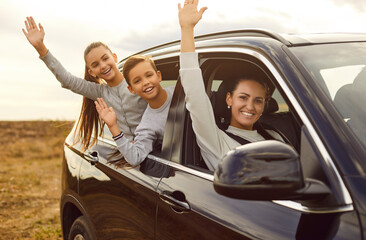 Portrait of happy smiling family waving hands with children sitting in modern car traveling by automobile together enjoying vacation or road trip on weekend. Family travel concept.