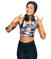 Beautiful hispanic woman wearing sportswear and headphones smiling cheerful showing and pointing with fingers teeth and mouth. dental health concept.