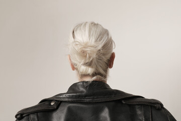 Back view headshot of blond woman wearing black jacket on white wall.