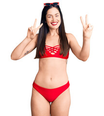 Young beautiful caucasian woman wearing bikini smiling looking to the camera showing fingers doing victory sign. number two.
