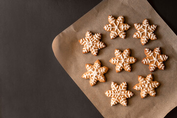 Christmas snowflake or star shape gingerbread cookie decorated with sugar icing on parchment on dark table background. Flat lay, copy space