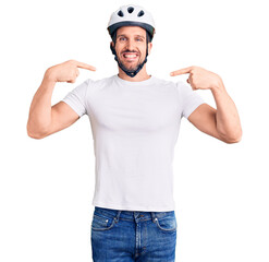 Young handsome man wearing bike helmet looking confident with smile on face, pointing oneself with...