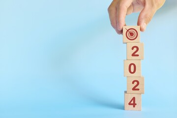 Year 2024 business target concept. Human hand stacking wooden blocks with 2024 target icon.