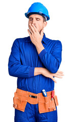 Young handsome man wearing worker uniform and hardhat bored yawning tired covering mouth with hand. restless and sleepiness.