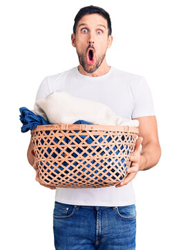Young handsome man holding laundry basket scared and amazed with open mouth for surprise, disbelief face