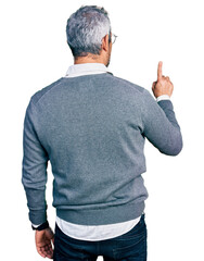 Middle age hispanic with grey hair wearing glasses posing backwards pointing ahead with finger hand