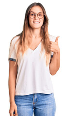 Beautiful caucasian woman wearing casual clothes and glasses smiling happy and positive, thumb up doing excellent and approval sign