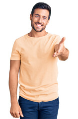 Young hispanic man wearing casual clothes smiling friendly offering handshake as greeting and welcoming. successful business.