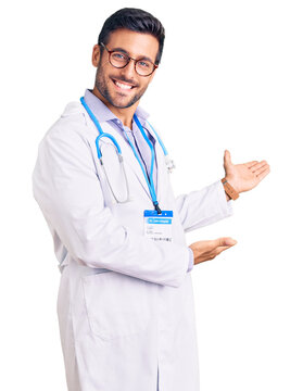 Young hispanic man wearing doctor uniform and stethoscope inviting to enter smiling natural with open hand