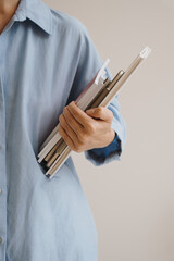 Woman in blue linen shirt holding office documents over white wall