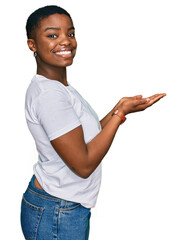 Young african american woman wearing casual white t shirt pointing aside with hands open palms...