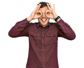 Young hispanic man wearing casual clothes doing ok gesture like binoculars sticking tongue out, eyes looking through fingers. crazy expression.