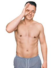 Handsome young man wearing swimwear shirtless doing ok gesture with hand smiling, eye looking through fingers with happy face.