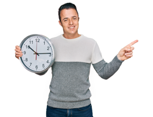 Handsome young man holding big clock smiling happy pointing with hand and finger to the side