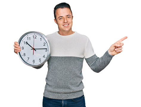 Handsome young man holding big clock smiling happy pointing with hand and finger to the side