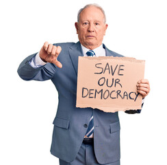 Senior handsome grey-haired man holding save our democracy cardboard banner with angry face, negative sign showing dislike with thumbs down, rejection concept