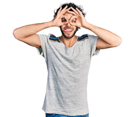 Fototapeta premium Young hispanic man wearing casual t shirt doing ok gesture like binoculars sticking tongue out, eyes looking through fingers. crazy expression.