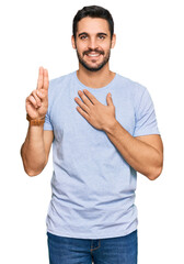 Fototapeta premium Young hispanic man wearing casual clothes smiling swearing with hand on chest and fingers up, making a loyalty promise oath