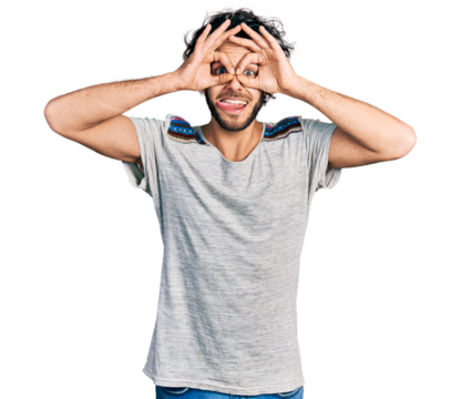 Young hispanic man wearing casual t shirt doing ok gesture like binoculars sticking tongue out, eyes looking through fingers. crazy expression.