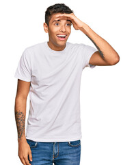 Young handsome african american man wearing casual white tshirt very happy and smiling looking far away with hand over head. searching concept.