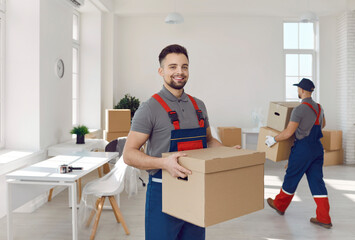 Young happy smiling employee of moving service in overall standing in the living room of new house...