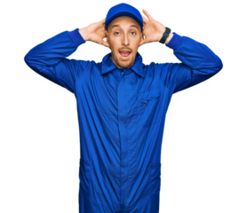 Bald man with beard wearing builder jumpsuit uniform crazy and scared with hands on head, afraid and surprised of shock with open mouth