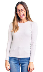 Beautiful brunette young woman wearing casual white sweater and glasses winking looking at the camera with sexy expression, cheerful and happy face.