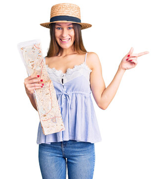 Beautiful brunette young woman wearing summer hat holding city map smiling happy pointing with hand and finger to the side