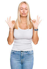 Young blonde girl wearing casual style with sleeveless shirt relaxed and smiling with eyes closed doing meditation gesture with fingers. yoga concept.